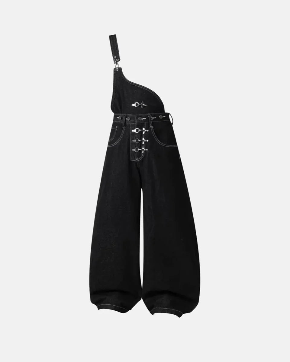 Salopette en jean asymétrique noire avec bretelle unique et boucles métalliques.